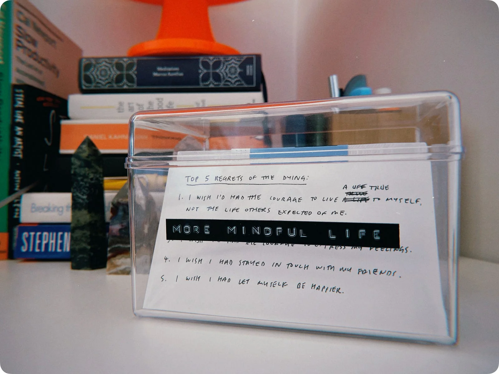 A clear index-card box on a desk, the front card handwritten with the top 5 regrets of the dying and a label reading “MORE MINDFUL LIFE”